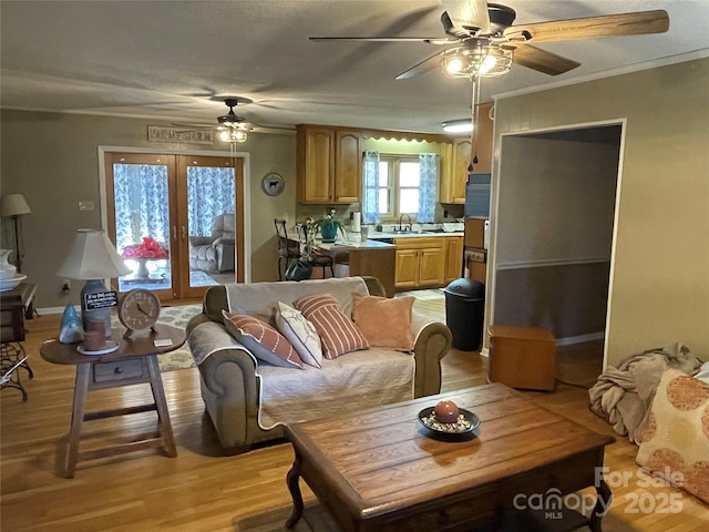 living room with sink, crown molding, ceiling fan, light hardwood / wood-style floors, and french doors