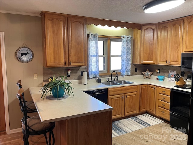 kitchen featuring sink, ornamental molding, black appliances, light hardwood / wood-style floors, and kitchen peninsula