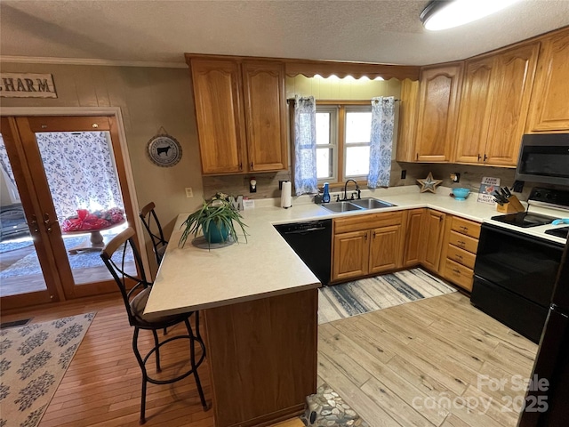 kitchen featuring sink, a kitchen bar, light hardwood / wood-style floors, black appliances, and crown molding