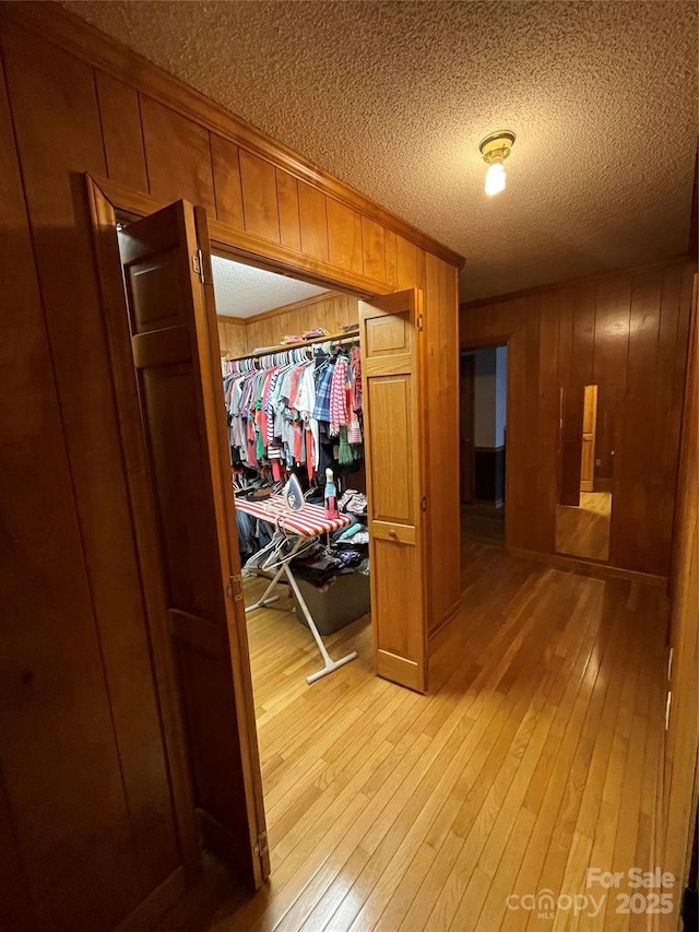 hall featuring crown molding, wooden walls, light hardwood / wood-style flooring, and a textured ceiling