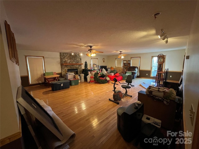 living room featuring a stone fireplace, a textured ceiling, track lighting, hardwood / wood-style flooring, and ceiling fan