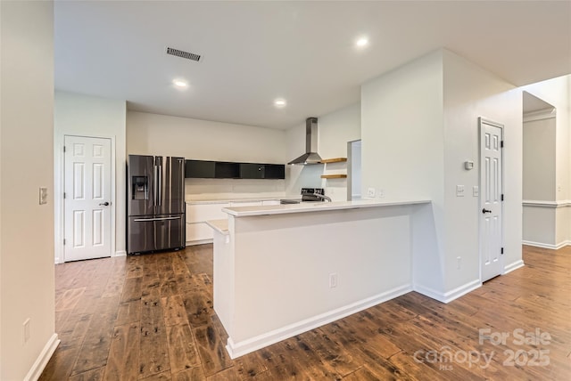 kitchen with dark hardwood / wood-style flooring, kitchen peninsula, appliances with stainless steel finishes, and wall chimney range hood