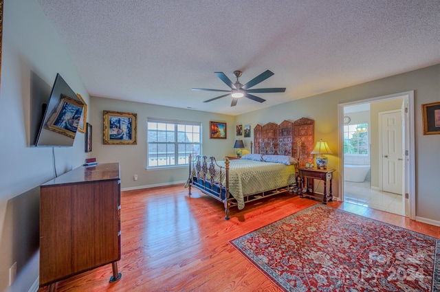 bedroom featuring ceiling fan, light wood-type flooring, a textured ceiling, and ensuite bath