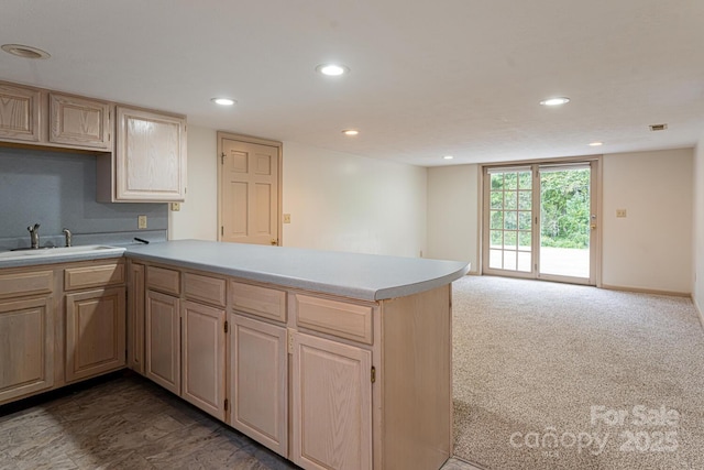 kitchen with kitchen peninsula, sink, light brown cabinetry, and dark carpet