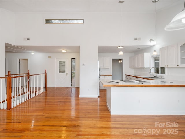 kitchen with kitchen peninsula, a towering ceiling, white cabinets, and decorative light fixtures