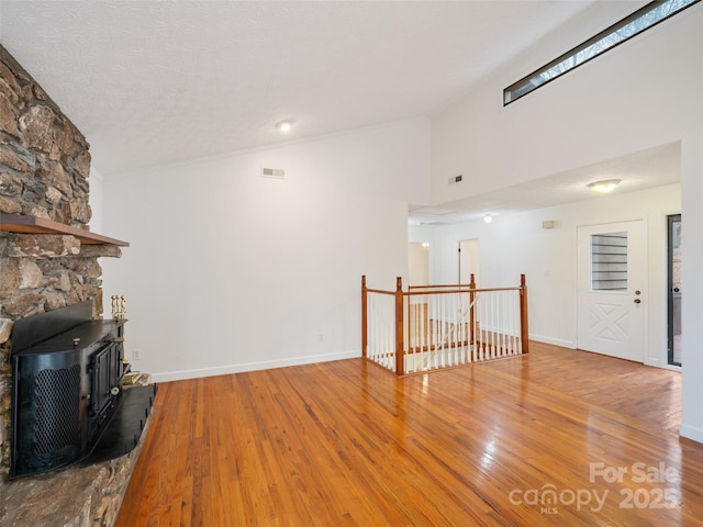 unfurnished living room with wood-type flooring, a textured ceiling, a wood stove, and lofted ceiling