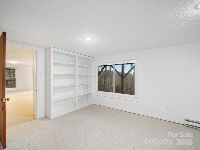 carpeted empty room with built in shelves, a textured ceiling, and baseboard heating