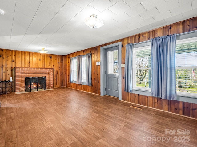 unfurnished living room featuring wood-type flooring, a brick fireplace, and wood walls