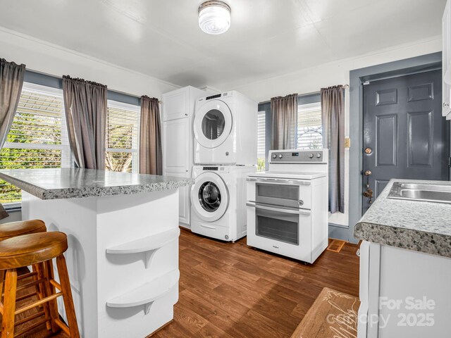 clothes washing area featuring sink, dark wood-type flooring, and stacked washer and clothes dryer