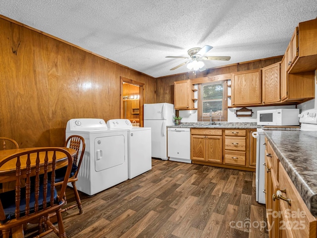 kitchen featuring washing machine and dryer, wood walls, sink, and white appliances