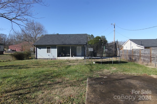 rear view of property with a yard, a trampoline, and a sunroom