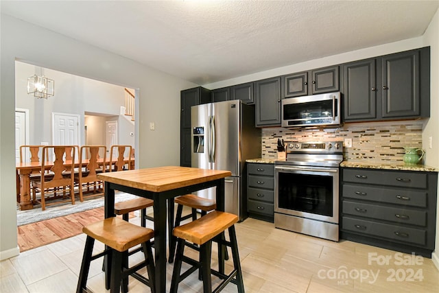 kitchen featuring light stone countertops, a textured ceiling, appliances with stainless steel finishes, tasteful backsplash, and a notable chandelier