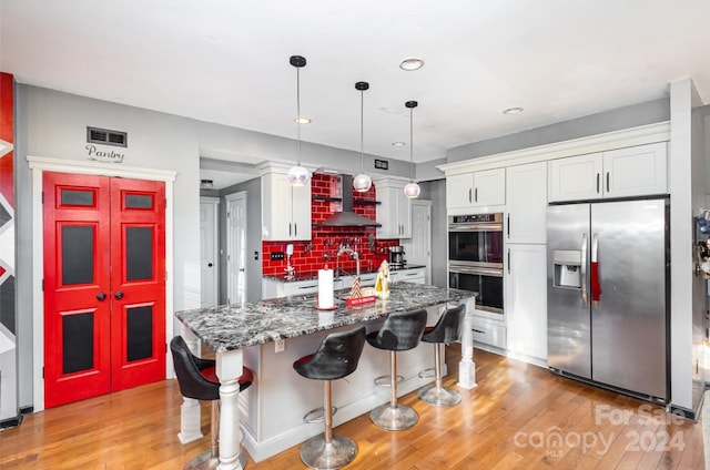 kitchen with a kitchen bar, wall chimney exhaust hood, stainless steel appliances, pendant lighting, and white cabinets