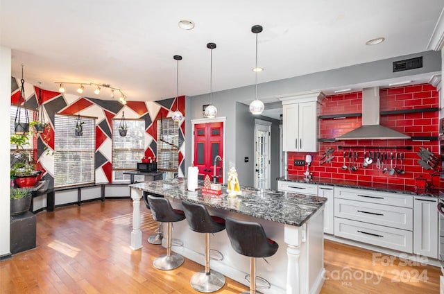 kitchen featuring white cabinets, pendant lighting, wall chimney exhaust hood, and sink