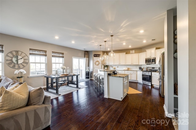 kitchen featuring hanging light fixtures, light stone countertops, an island with sink, appliances with stainless steel finishes, and a breakfast bar area