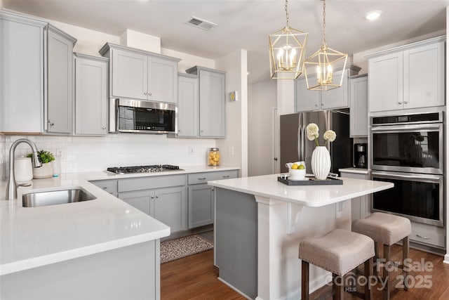 kitchen featuring sink, gray cabinets, a kitchen island, stainless steel appliances, and decorative backsplash