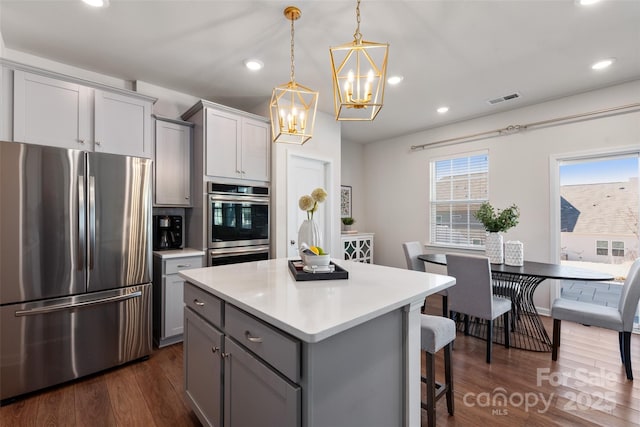 kitchen with gray cabinets, appliances with stainless steel finishes, dark hardwood / wood-style floors, a kitchen bar, and hanging light fixtures