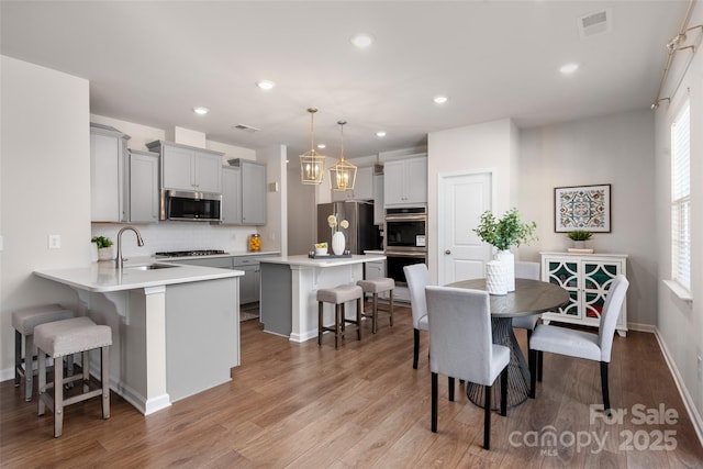 kitchen featuring a breakfast bar area, gray cabinetry, hanging light fixtures, kitchen peninsula, and stainless steel appliances