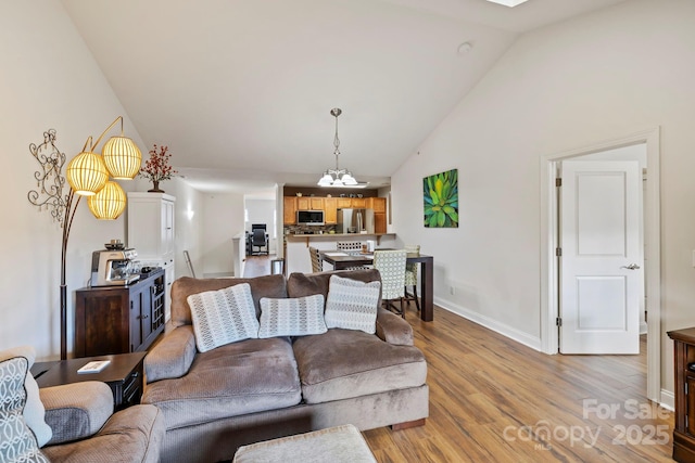 living room with light hardwood / wood-style floors, vaulted ceiling, and a notable chandelier