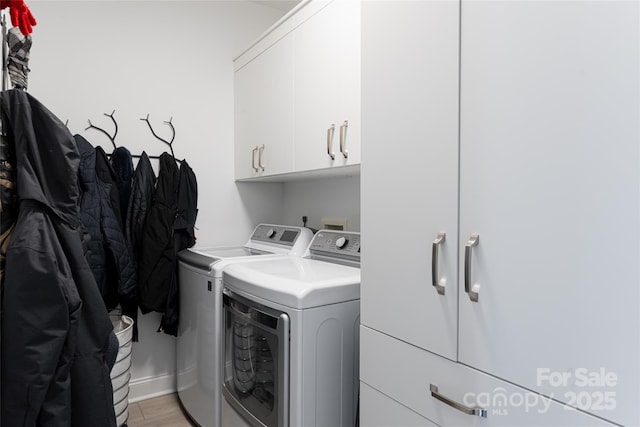 laundry area with cabinets, washing machine and dryer, and light hardwood / wood-style flooring