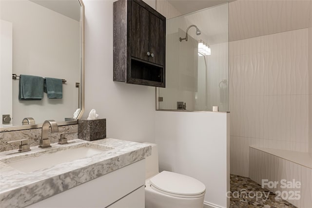 bathroom featuring a tile shower, vanity, and toilet