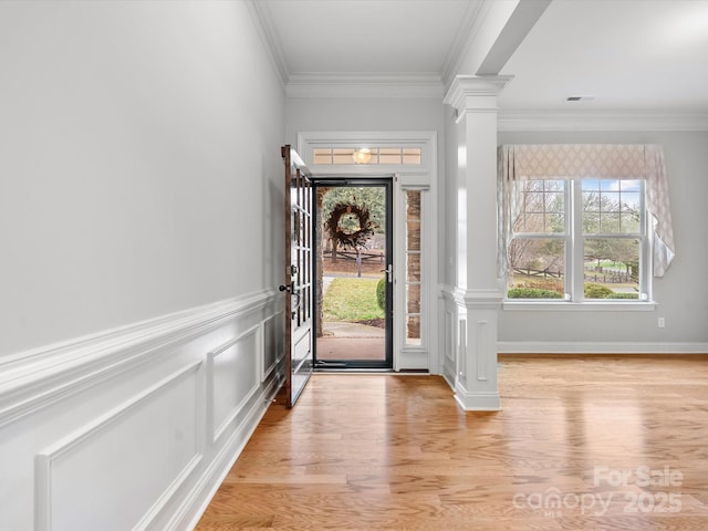 entrance foyer featuring a wainscoted wall, crown molding, decorative columns, light wood finished floors, and a decorative wall