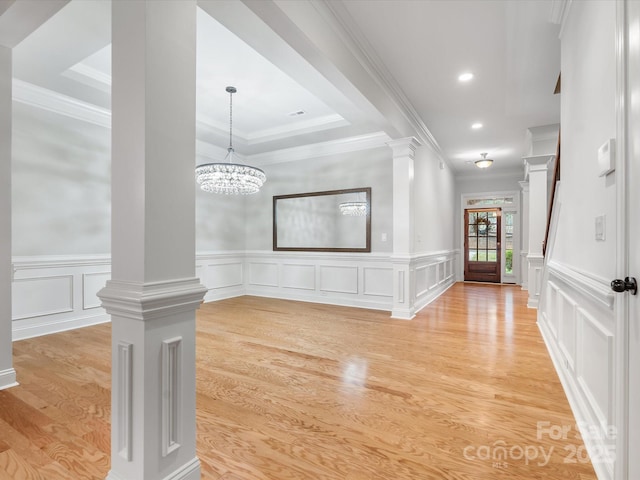 foyer entrance featuring light wood-style floors, crown molding, and ornate columns