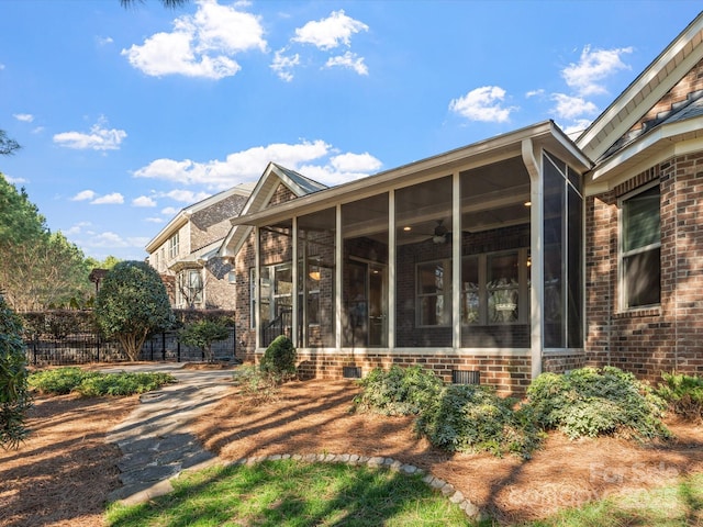 exterior space featuring brick siding, crawl space, fence, and a sunroom