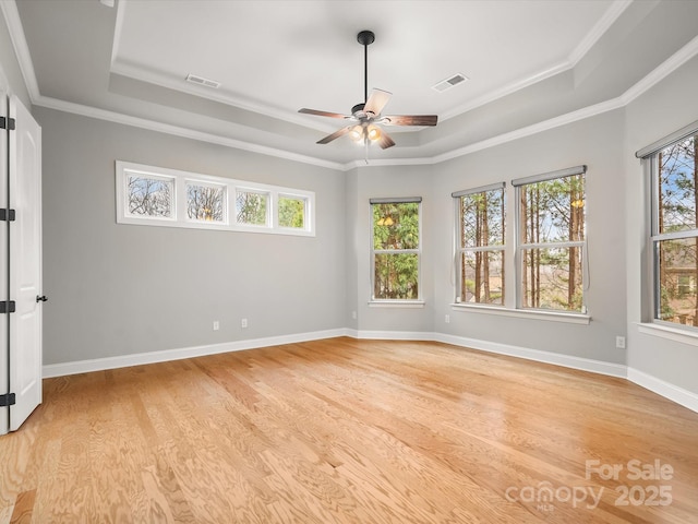 empty room with light wood-type flooring, a raised ceiling, visible vents, and baseboards