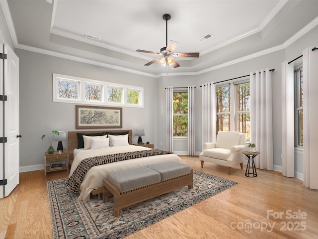 bedroom featuring a tray ceiling, visible vents, light wood-style flooring, and baseboards