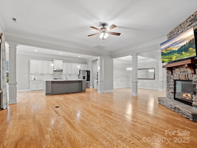 unfurnished living room with a ceiling fan, decorative columns, a stone fireplace, and ornamental molding