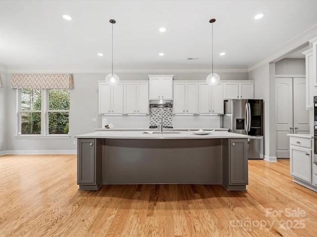 kitchen featuring under cabinet range hood, a kitchen island with sink, stainless steel refrigerator with ice dispenser, and light countertops