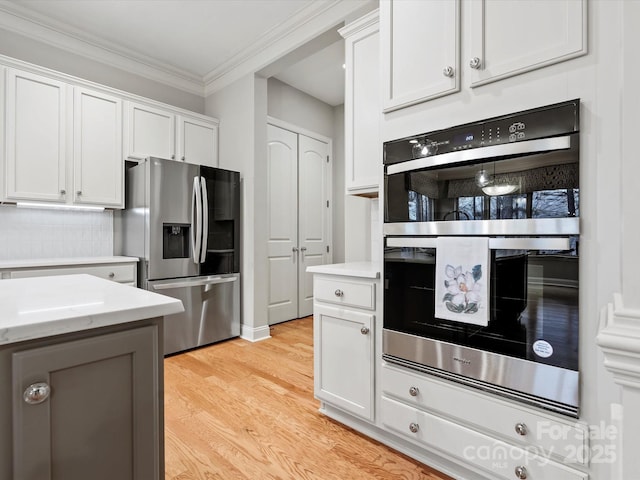 kitchen featuring decorative backsplash, white cabinets, appliances with stainless steel finishes, crown molding, and light wood-style floors