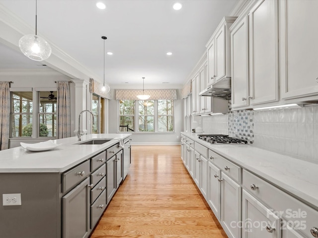 kitchen featuring gray cabinetry, a sink, light countertops, stainless steel gas stovetop, and crown molding