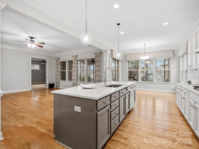 kitchen with light wood finished floors, gray cabinets, crown molding, light countertops, and a sink