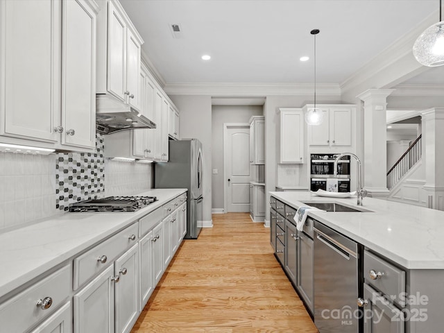 kitchen featuring under cabinet range hood, stainless steel appliances, a sink, ornamental molding, and decorative columns