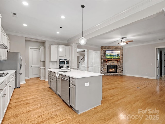 kitchen with a stone fireplace, gray cabinetry, stainless steel appliances, visible vents, and light wood-style floors