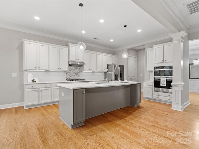 kitchen with under cabinet range hood, a sink, visible vents, appliances with stainless steel finishes, and light wood finished floors