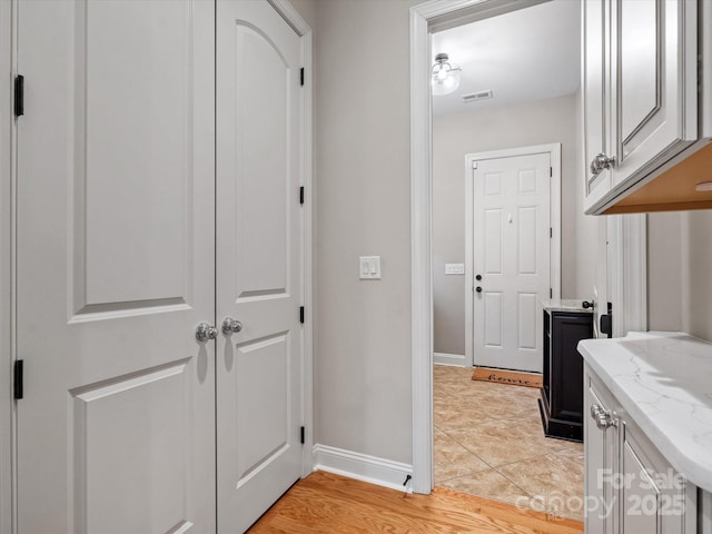 corridor featuring baseboards, visible vents, and light tile patterned flooring