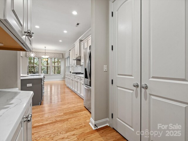 kitchen featuring stainless steel fridge, visible vents, hanging light fixtures, light wood-type flooring, and gas stovetop