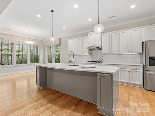 kitchen with under cabinet range hood, ornamental molding, visible vents, and stainless steel fridge with ice dispenser