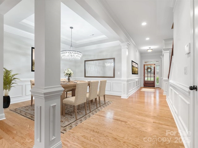 dining space featuring crown molding, light wood-type flooring, a decorative wall, and decorative columns