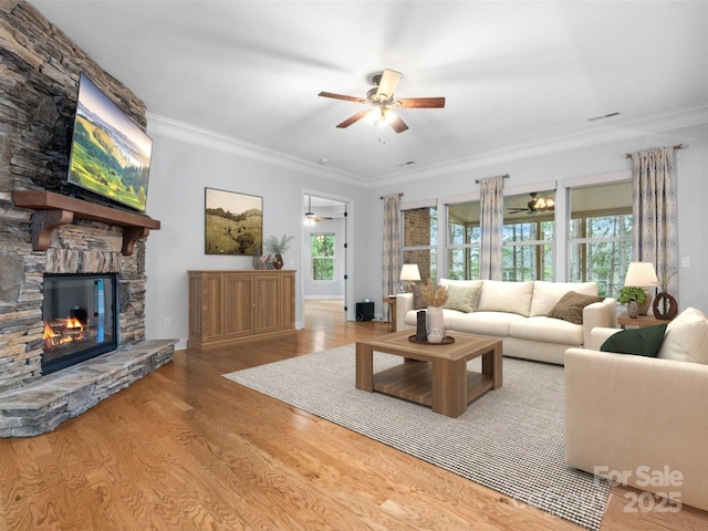 living room featuring ceiling fan, crown molding, a stone fireplace, and wood finished floors