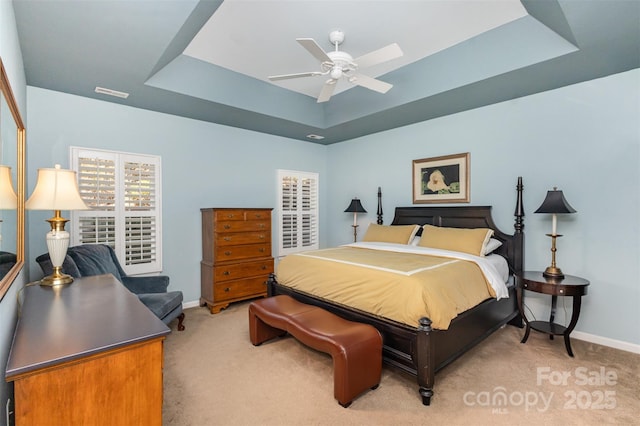 bedroom with ceiling fan, a tray ceiling, and light carpet