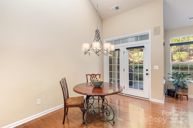 dining room with wood-type flooring, vaulted ceiling, and an inviting chandelier