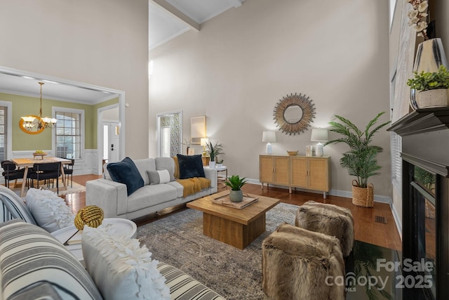 living room featuring a chandelier, wood-type flooring, ornamental molding, and a high ceiling