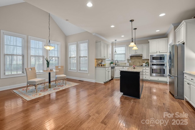 kitchen with a center island, white cabinets, decorative light fixtures, light stone counters, and stainless steel appliances