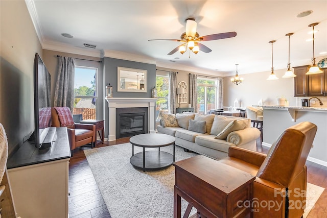 living room with ceiling fan with notable chandelier, dark hardwood / wood-style floors, ornamental molding, and sink