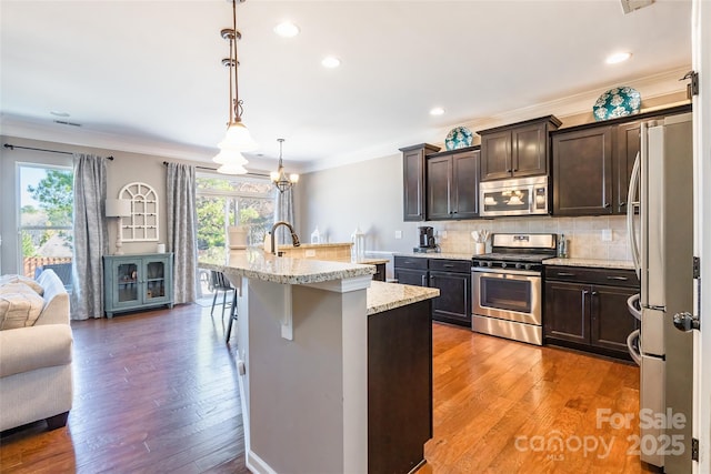 kitchen with dark brown cabinetry, hanging light fixtures, a kitchen bar, a center island with sink, and appliances with stainless steel finishes