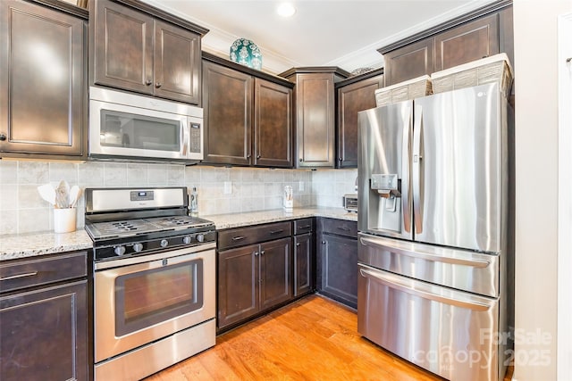 kitchen with tasteful backsplash, light stone counters, dark brown cabinets, stainless steel appliances, and light hardwood / wood-style flooring